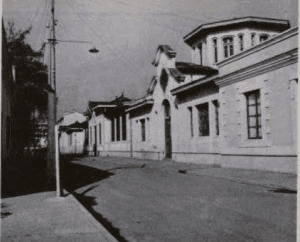 Imagen en blanco y negro del frontis del edificio de la Biblioteca desde una esquina. El edificio tiene una arquitectura colonial, con un primer piso y un torreón. Se ve la calle vacía.