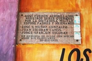 Placa de mármol café ubicada al costado izquierdo del memorial, allí se lee en letras pintadas negras: Aquí fueron acribillados nuestros seres queridos por la dictadura militar, esposo, padres y hermanos: José S. Muñoz González, Juan Escobar Camus, Jorge Oyarzún Escobar. En memoria de ellos con mucho amor sus familiares. 30 de Septiembre de 1973. Al costado derecho de la placa se ven fotografías de hombres desteñidas.