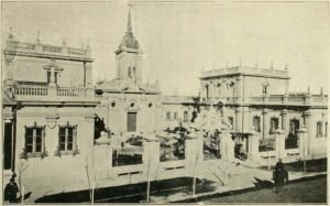 Imagen en blanco y negro de los edificios, de izquierda a derecha, de la Gota de Leche, Iglesia Santa Lucrecia y Casa de acogida. El primero y el tercero son idénticos en su construcción. En el centro de las tres construcciones hay una plazoleta. En la esquina inferior derecha se observa un guardia a caballo.