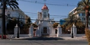 Frontis actual de la Iglesia Santa Lucrecia. En el centro se observa la cúpula de la parroquia. A los costados están el ala izquierda y derecha de la parroquia con dos ventanas cada una. En frente de la edificación se encuentra una pileta de mármol y la iglesia está flanqueada por dos palmeras.