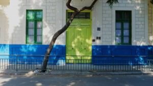 Frontis de la escuela de hombres en la actualidad. El edificio tiene un piso, es de hormigón armado y está pintado en blanco y azul, la puerta principal es verde claro y las ventanas verde oscuro con rejillas. En primer plano se ve la calle y una reja verde a lo largo de la vereda.