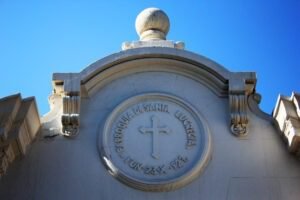 Detalle del frontis de la iglesia, que consiste en un círculo y una cruz tallados en el material de construcción y en donde se lee: Parroquia de Santa Lucrecia, Fundada 23 de octubre de 1927.