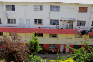 Fotografía actual de un bloque de departamentos al interior de la Población Huemul III. Los departamentos son de dos pisos. Hay árboles en el patio interior.