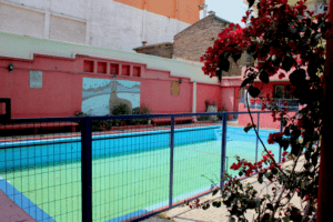 Fotografía actual de una piscina al interior de la Población Huemul III. No tiene agua y es de color celeste. Al fondo, en una pared, se observa un mural con un huemul y araucarias.