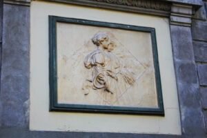 Detalle de un sobre relieve de dos personas de aspecto femenino en uno de los muros laterales del teatro. Tienen un color neutro, similar al beige y están esculpidas de perfil, una mujer en primer plano y la otra a un costado de esta, en segundo plano.